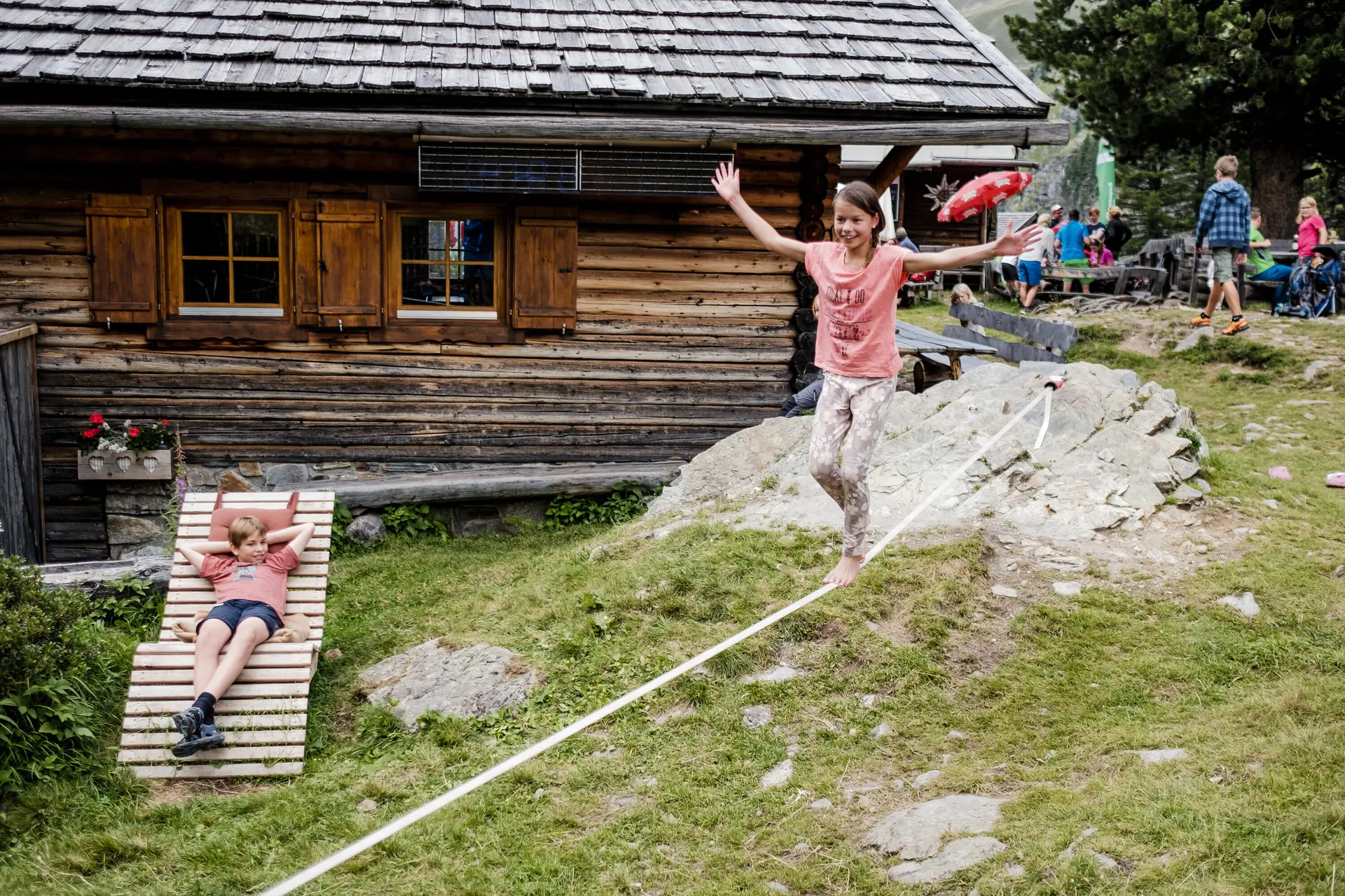 Zwei Kinder balancieren auf einem Seil, das vor einer Berghütte gespannt ist | © DAV/Hans Herbig