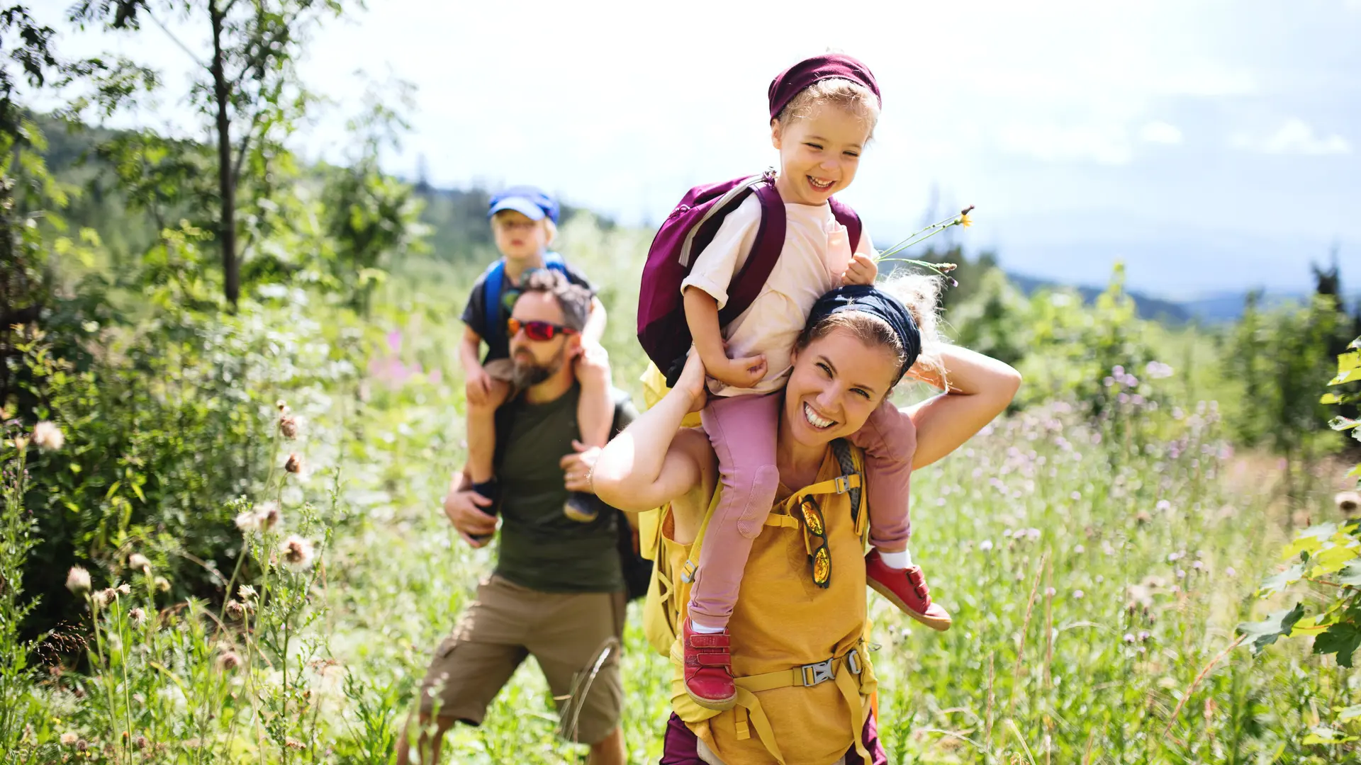 Eine Familie in der Natur, die Mutter trägt ein Kind auf den Schultern | © Halfpoint / Adobe Stock