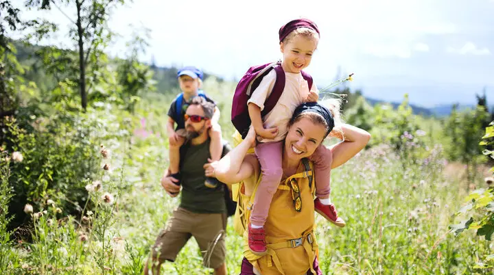 Eine Familie in der Natur, die Mutter trägt ein Kind auf den Schultern | © Halfpoint / Adobe Stock