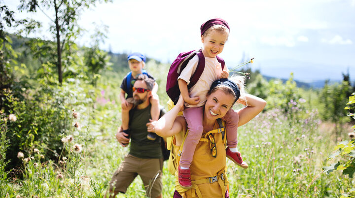 Eine Familie in der Natur, die Mutter trägt ein Kind auf den Schultern | © Halfpoint / Adobe Stock